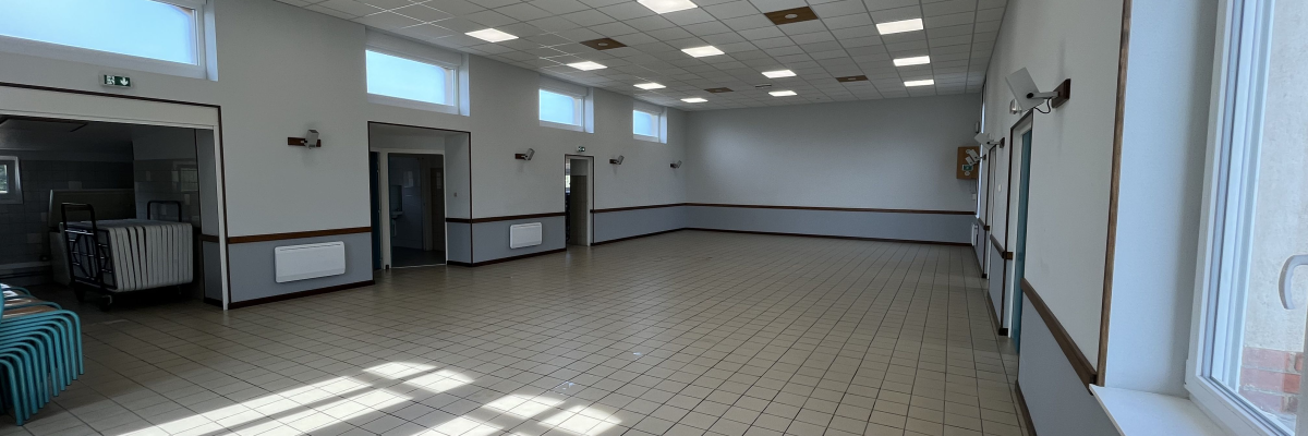 Salle vide avec carrelage, fenêtres, portes, radiateurs et éclairage au plafond.