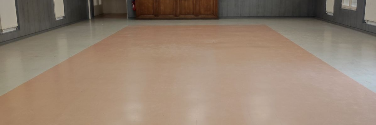 Salle vide avec sol en bois, murs blancs, éclairage, porte et placard.