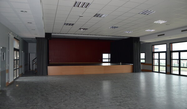 Salle vide avec un bar, des fenêtres, des plafonniers et une scène.