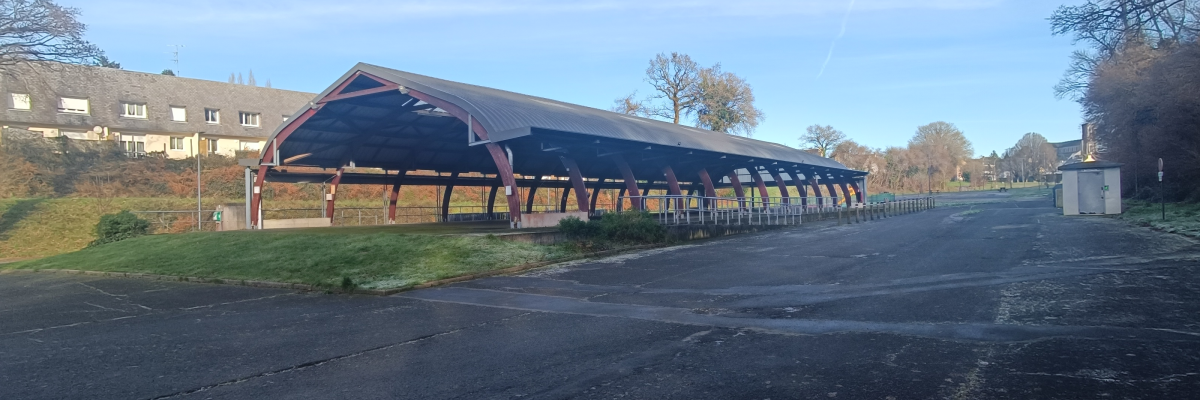 Structure couverte avec bancs et bâtiment en arrière-plan.