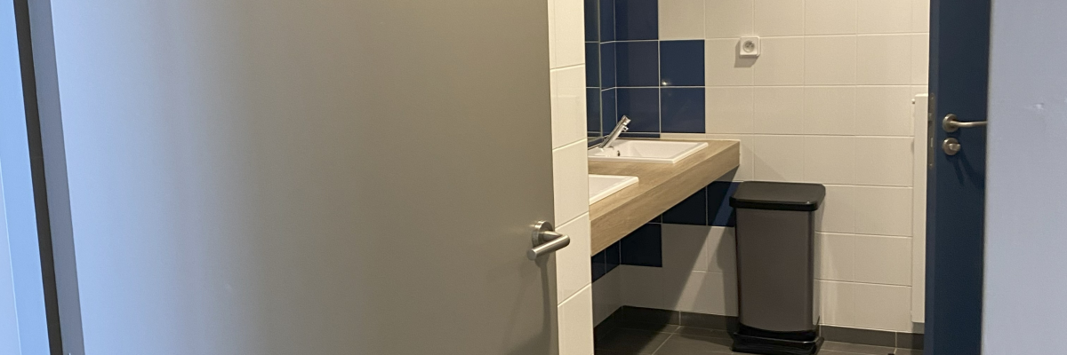 Petite salle avec porte ouverte, évier, poubelle et carrelage bleu.