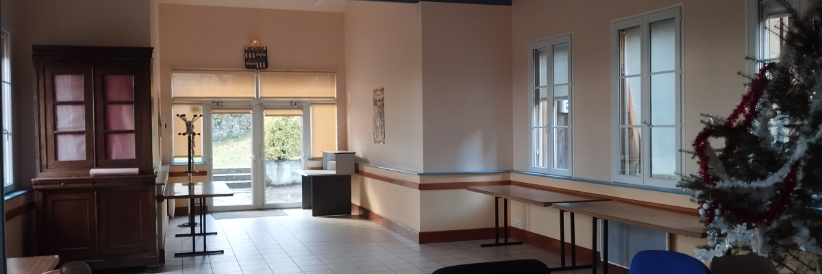 Salle avec tables, chaises, comptoir, sapin de Noël et horloge murale.