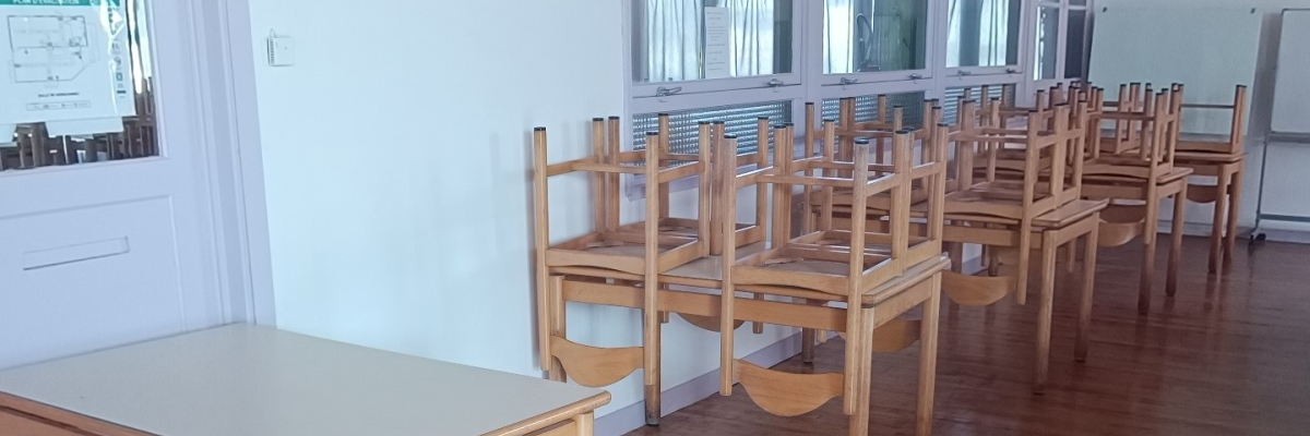 Salle de classe avec tables, chaises, tableau blanc et fenêtre.