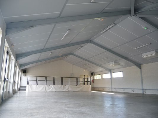 Salle vide sous toit, sol en béton, murs blancs, portes et fenêtres, éclairage au plafond.