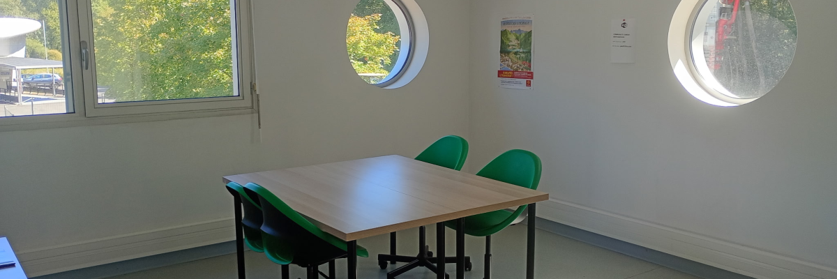 Salle avec table, chaises, fenêtres rondes et rectangulaire, affiches.