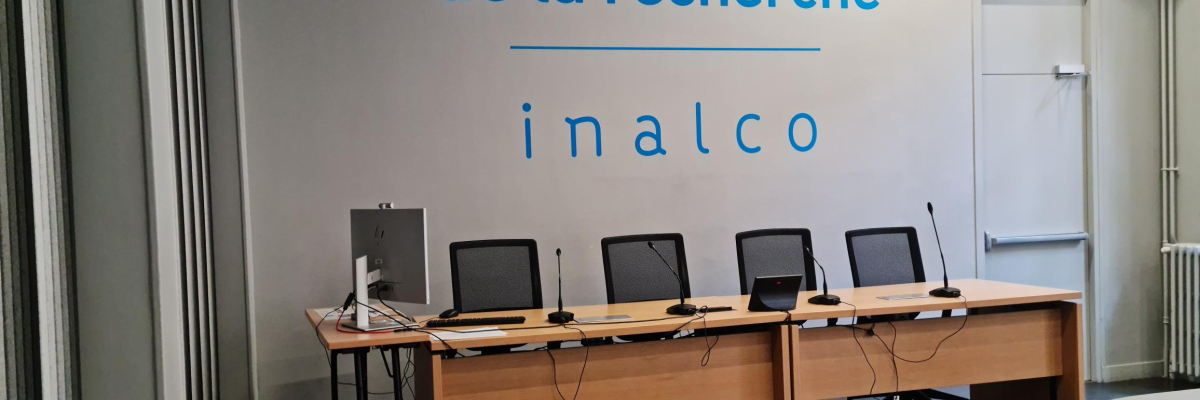 Salle de conférence avec écrans, microphones et chaises. Mur avec texte "Maison de la recherche inalco".