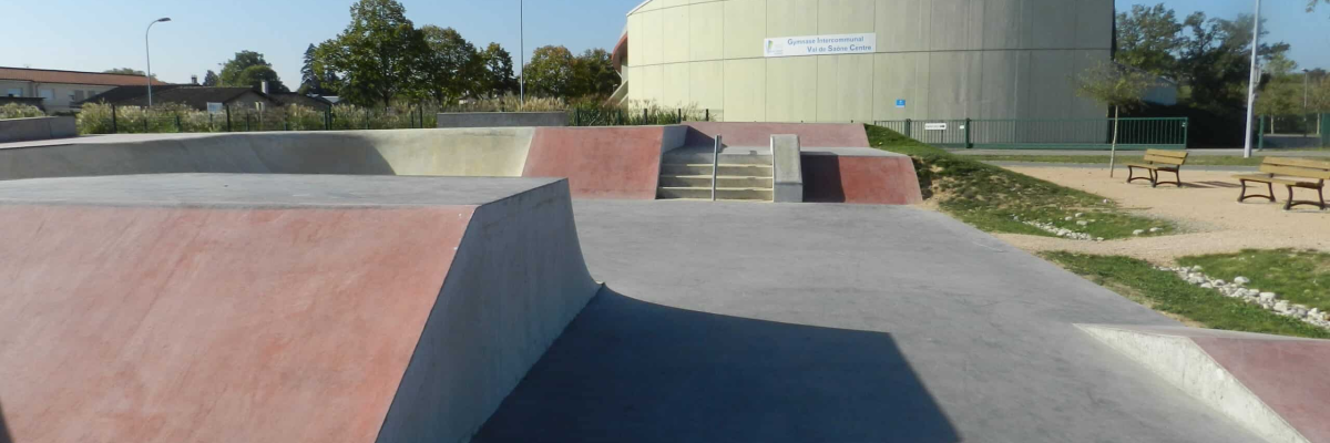 Skatepark avec rampe, éclairage, bancs, et bâtiment en arrière-plan.