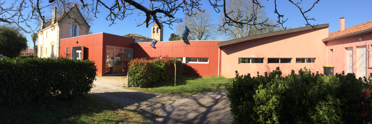 Bâtiment avec entrée, arbres, buissons, ciel bleu.