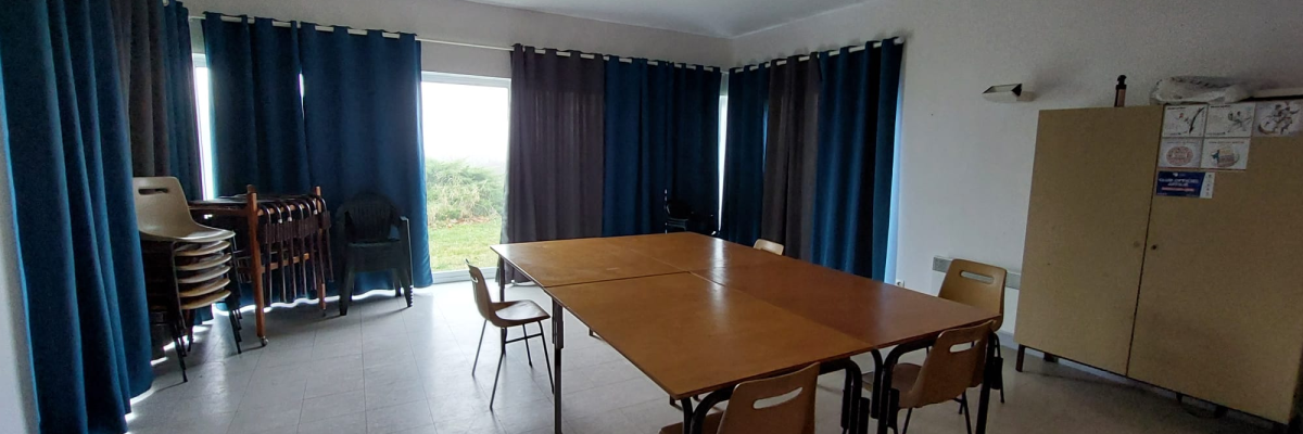 Salle avec table, chaises, armoire et fenêtres avec rideaux.