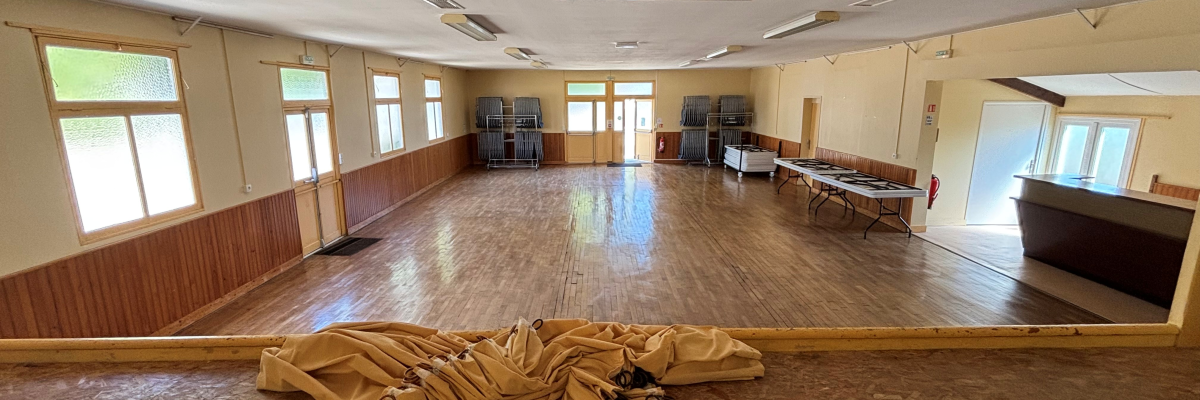 Salle avec parquet, tables, chaises, et rideaux.