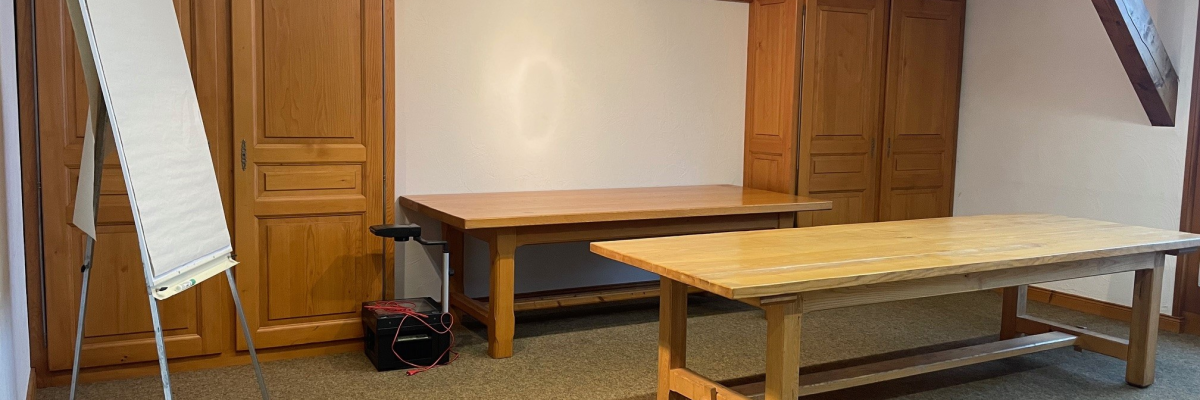 Salle de réunion avec tableau, deux tables, et armoires.