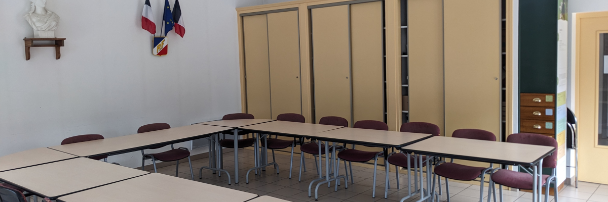 Salle avec tables, chaises, armoires, tableau et drapeau.