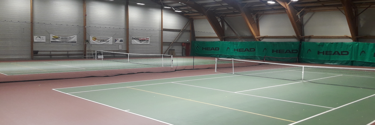 Terrain de tennis intérieur avec filets, éclairage et publicités murales.