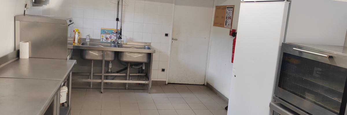 Cuisine avec plans de travail en acier inoxydable, évier, réfrigérateur, four et porte.