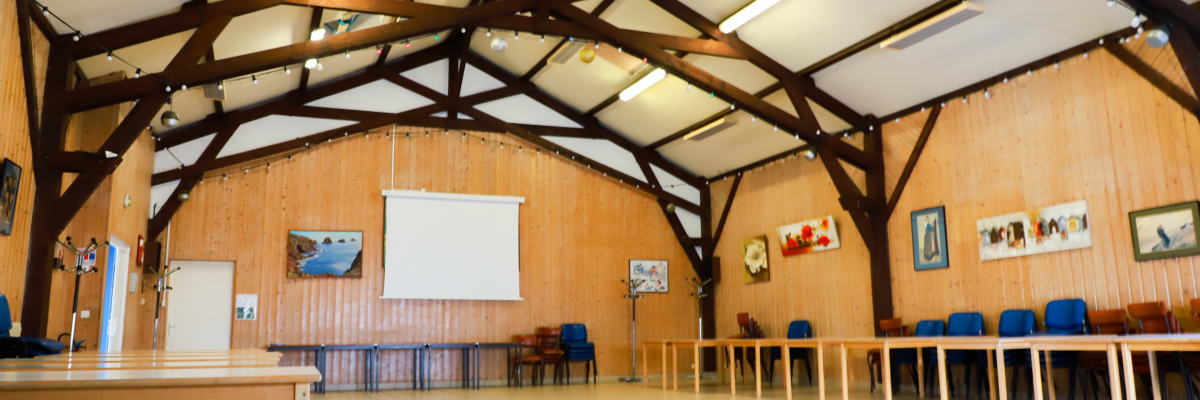 Salle avec tables, chaises, écran blanc et tableaux aux murs.