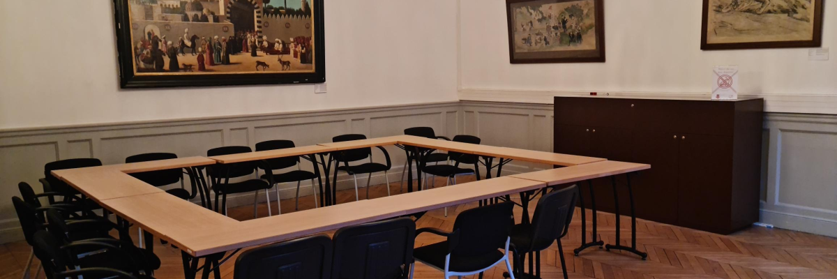 Salle avec table, chaises, lustre, tableaux et armoire.