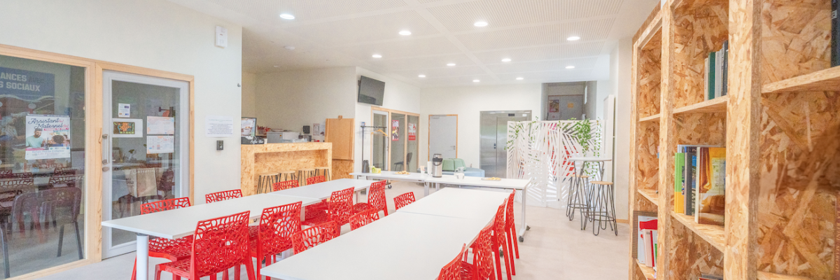Salle avec tables, chaises rouges, bibliothèques, plantes et porte vitrée.