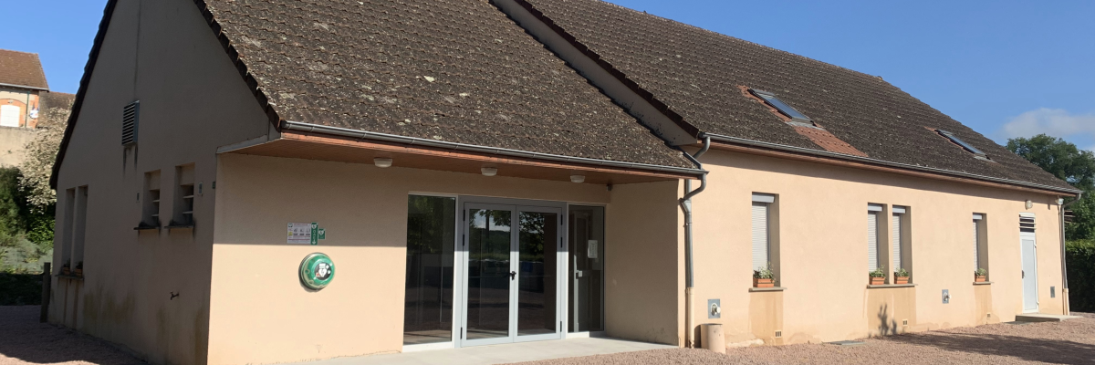 Bâtiment avec toît pentu, portes vitrées, fenêtres, panneau et gravier.