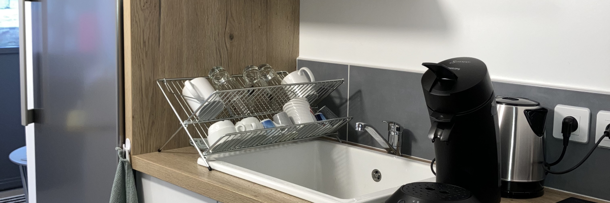 Cuisine : évier, micro-ondes, cafetière, torchons, placards, plaque de cuisson, réfrigérateur.