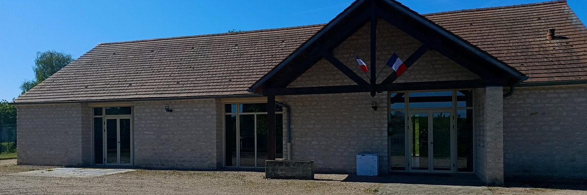 Bâtiment avec toiture en tuiles, murs en briques, grandes fenêtres et portes vitrées. Deux drapeaux français.