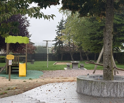 Aire de jeux avec toboggan, bac à sable, et arbre.
