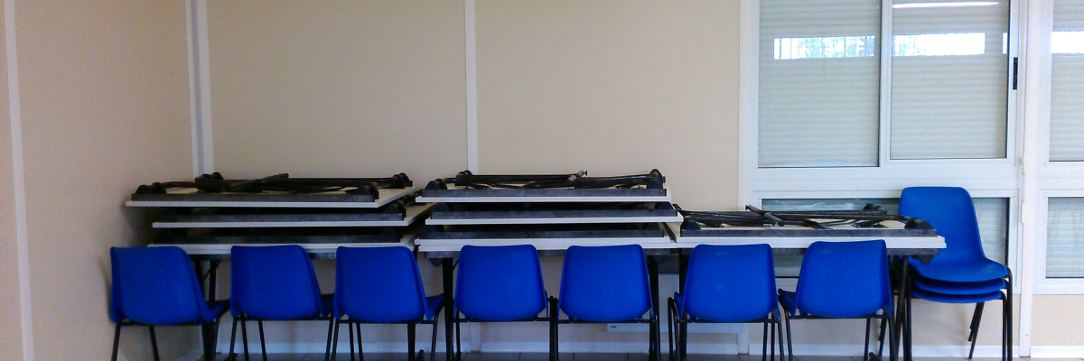 Pièces empilées sur tables, chaises bleues, porte vitrée.