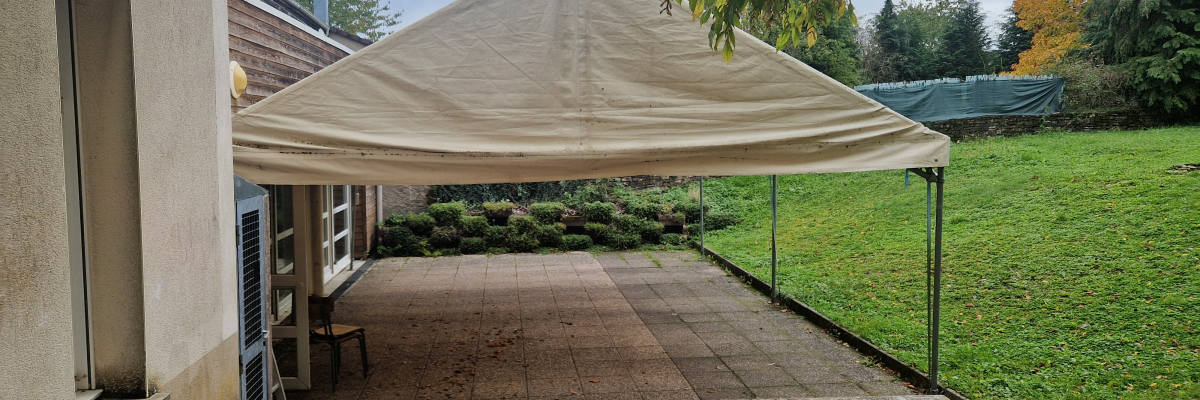 Tente blanche, bâtiment, terrasse pavée, pelouse, arbres.