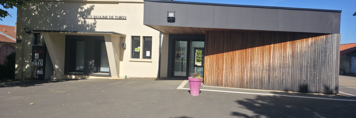 Bâtiment avec entrée principale, porte vitrée, panneau d'affichage et pot de fleurs.