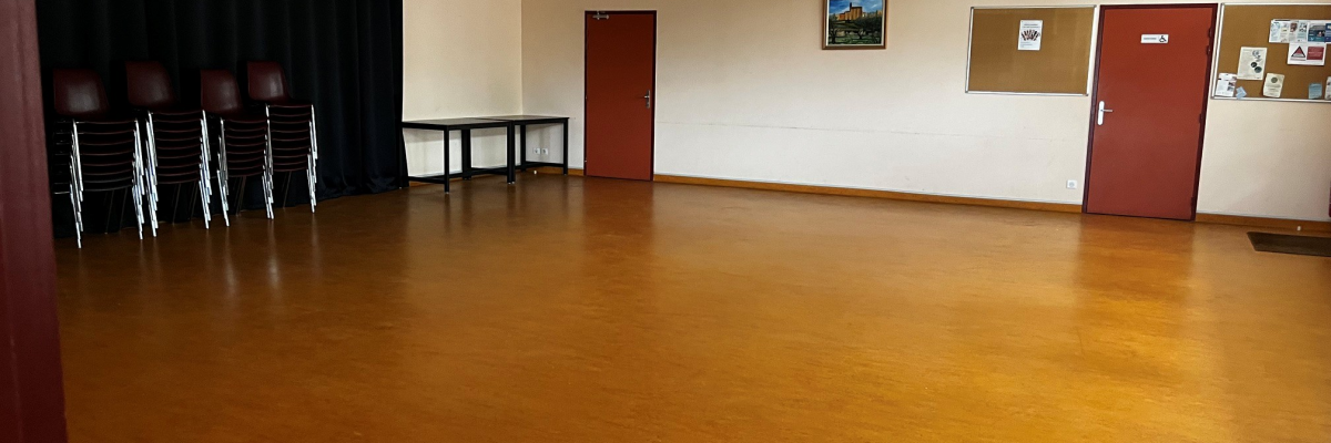 Salle avec chaises empilées, table, porte rouge, tableau d'affichage et rideau noir.