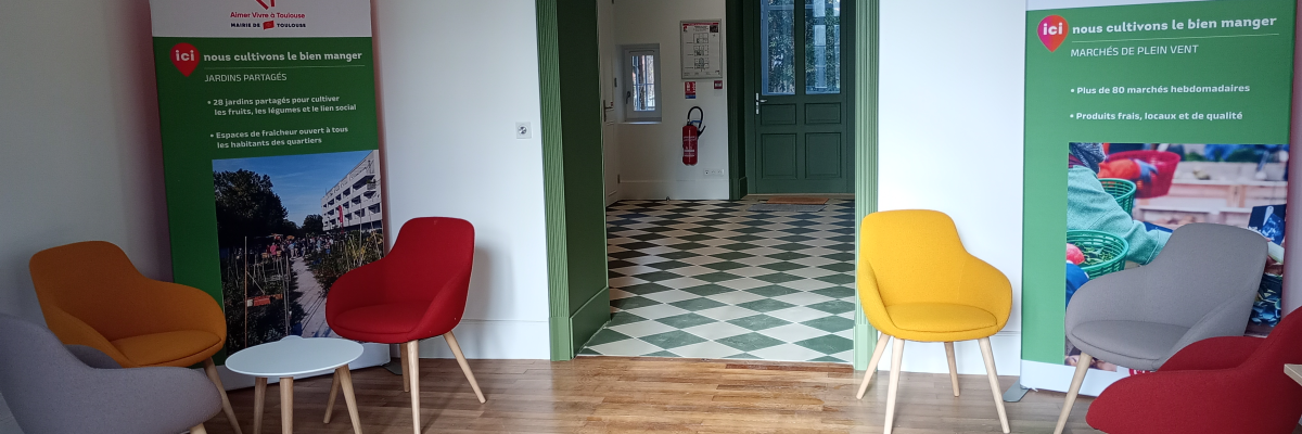 Salle d'attente avec chaises colorées, tables basses, panneaux d'affichage et porte verte.