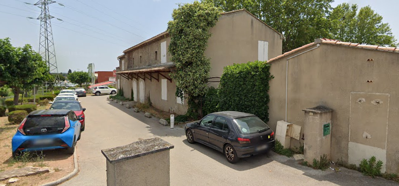 Rue avec voitures garées, bâtiments et végétation.