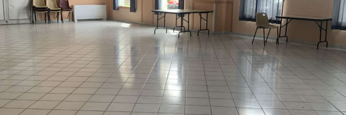 Salle avec tables, chaises, fenêtres et sol carrelé.