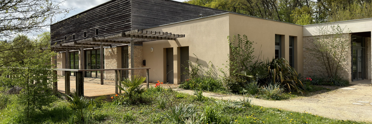 Maison moderne avec toit plat, murs beiges, grandes fenêtres et jardin bien entretenu.