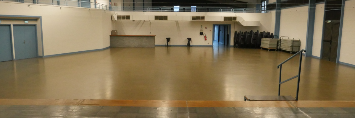 Grande salle avec sol lisse, éclairage suspendu, rampes et escalier métallique.