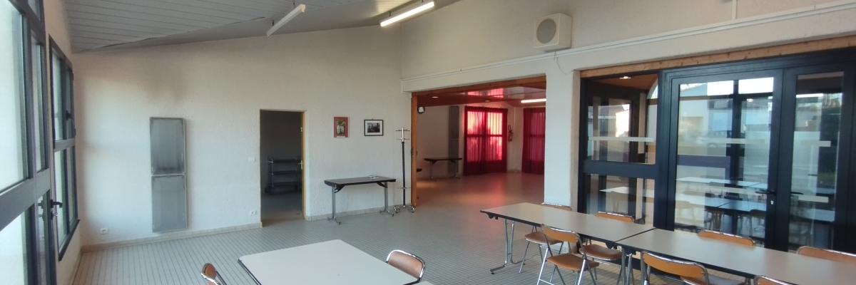 Salle avec tables, chaises, frigo, porte, fenêtres et lumières au plafond.