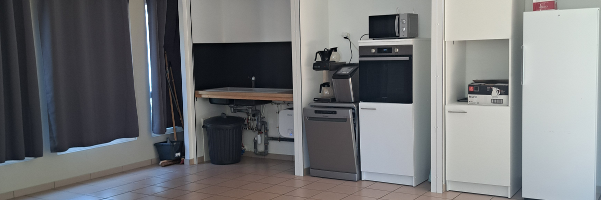 Cuisine avec sol carrelé, réfrigérateur, four, micro-ondes, télévision et poubelle.