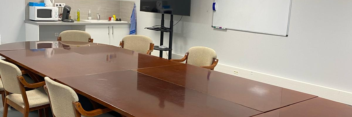Salle de réunion avec table, chaises, tableau blanc, télévision et micro-ondes.