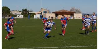 Match de rugby avec joueurs en action, portant des maillots rouges et bleus, sur un terrain herbeux.