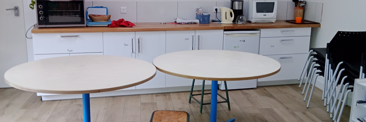 Salle avec tables rondes, tabourets, cuisine équipée et décorations en papier.