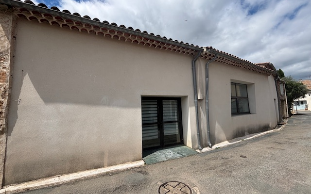 Maison avec toiture de tuiles, porte et fenêtre. Rue pavée avec regard.