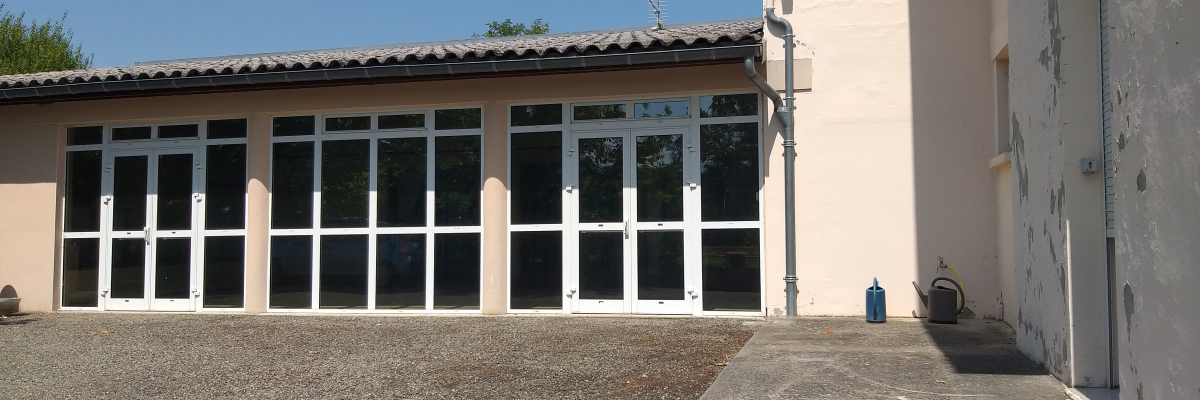 Bâtiment avec grandes portes vitrées, cour de gravier, mur adjacent.