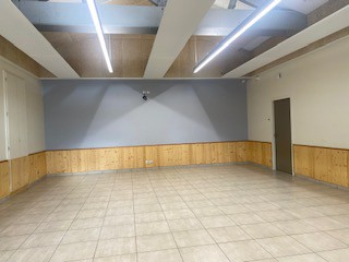 Salle vide avec murs partiellement en bois, carrelage, plafond à poutres apparentes et éclairage intégré.