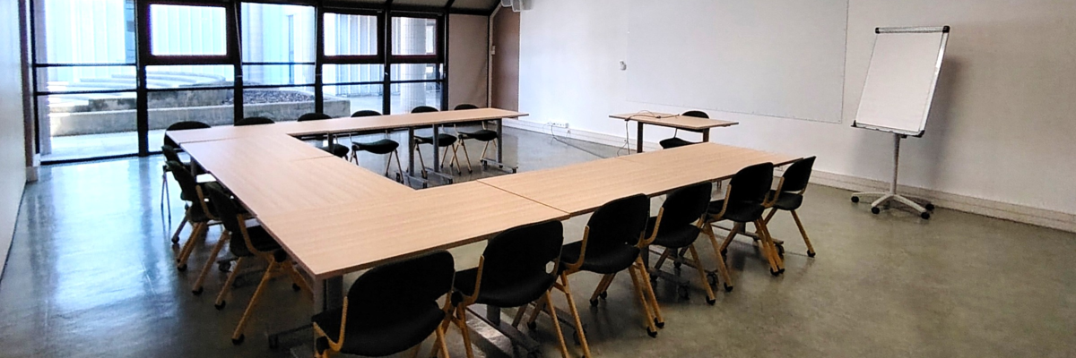 Salle avec tables en U, chaises, tableau blanc et vidéoprojecteur.