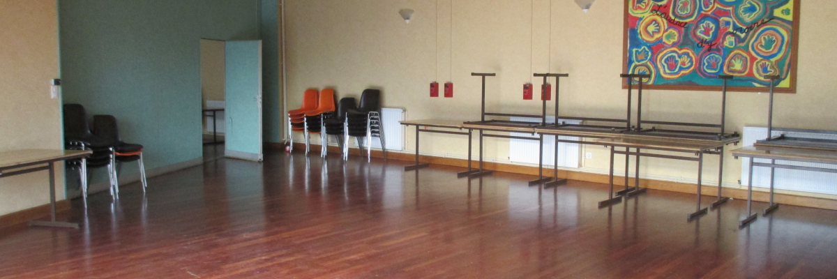 Salle avec plancher en bois, chaises, tables, tableau mural et éclairage au plafond.