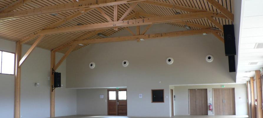 Grande salle avec poutre en bois, sol nu, portes et écrans.