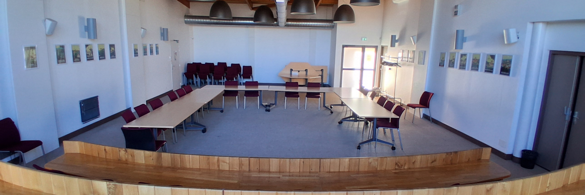 Salle avec tables, chaises, luminaires suspendus, tableaux et porte.