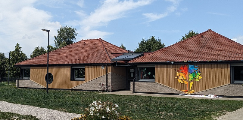Bâtiment avec toiture rouge, panneaux solaires, vélo, graffiti mural et fleurs.