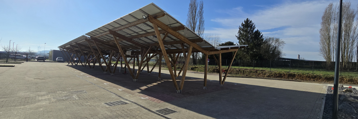 Parking avec abris à panneaux solaires, lampadaire et véhicules en arrière-plan.