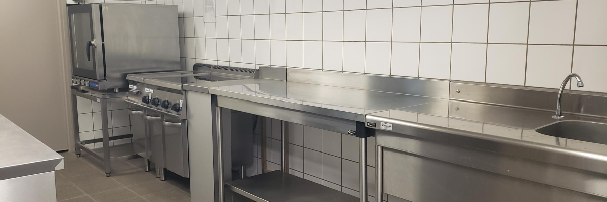 Cuisine avec plans de travail, évier, four, plaque de cuisson et étagère métallique.