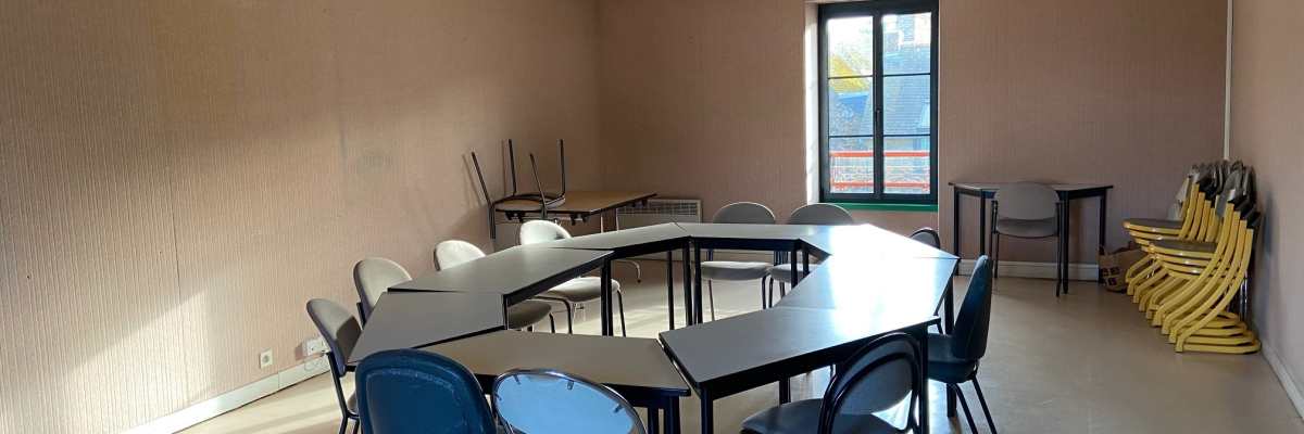 Salle de réunion avec tables, chaises, ventilo-convecteurs et meuble de rangement.